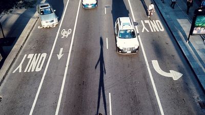 High angle view of a woman crossing a road. City streets, asphalt, bike lanes, car traffic, pedestrians