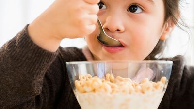 Little girl eating a bowl of cereal with milk. Cheerios Breakfast