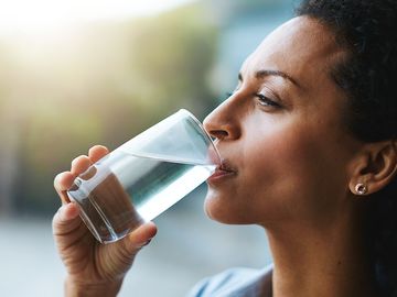 Shot of a woman drinking a glass of water at home. Drink sip hydration